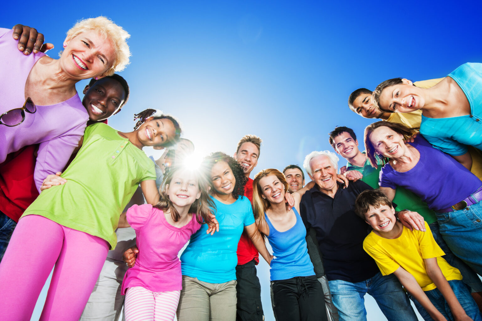 Group of embraced people standing against blue sky.